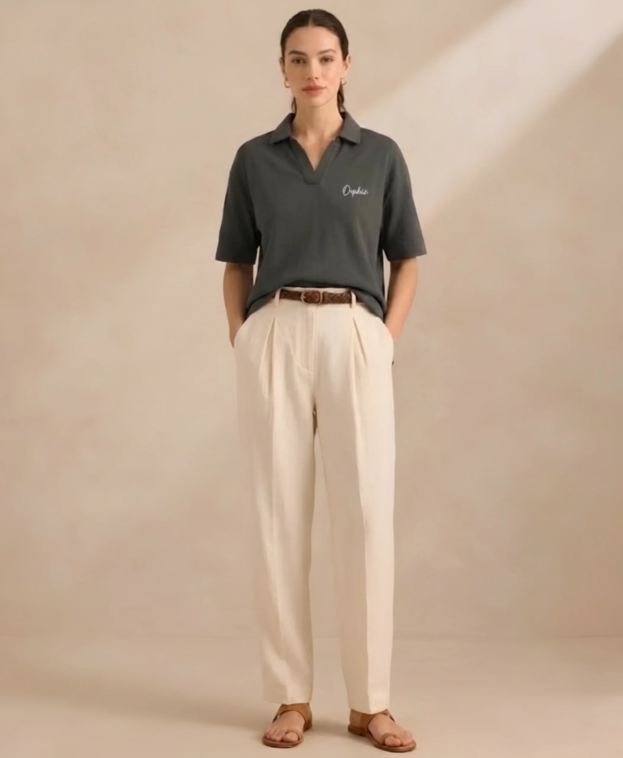 Woman wearing Orphic charcoal open-collar polo, front view with cream trousers.webp