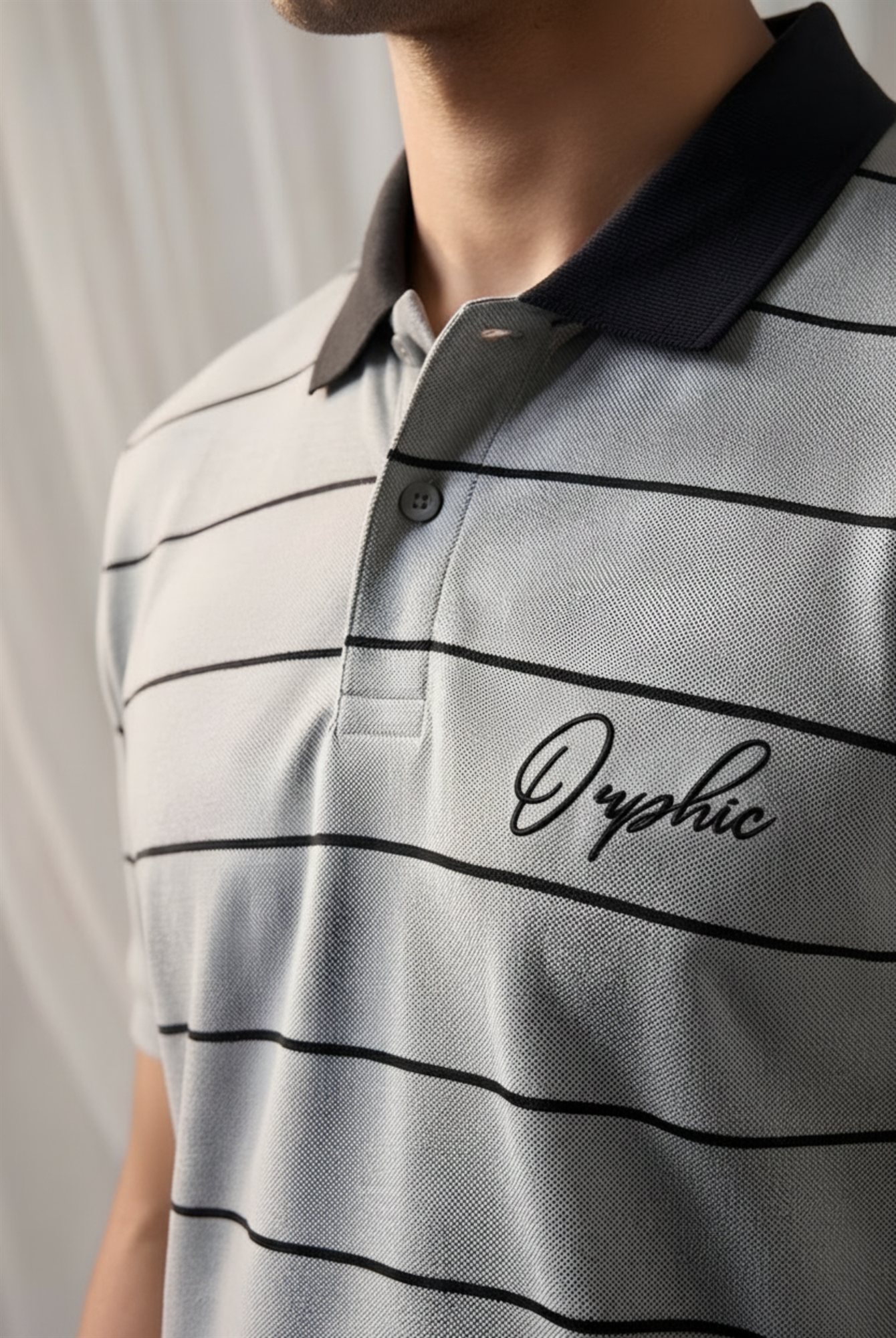 Close-up of Orphic men's grey striped polo showing black collar and chest embroidery