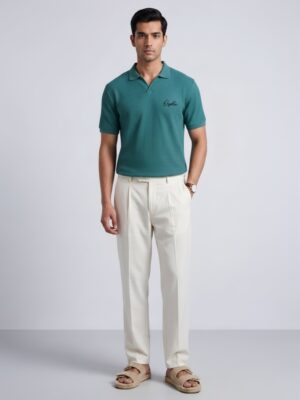 Model wearing Orphic men's teal waffle-knit polo with open collar, front view with cream trousers