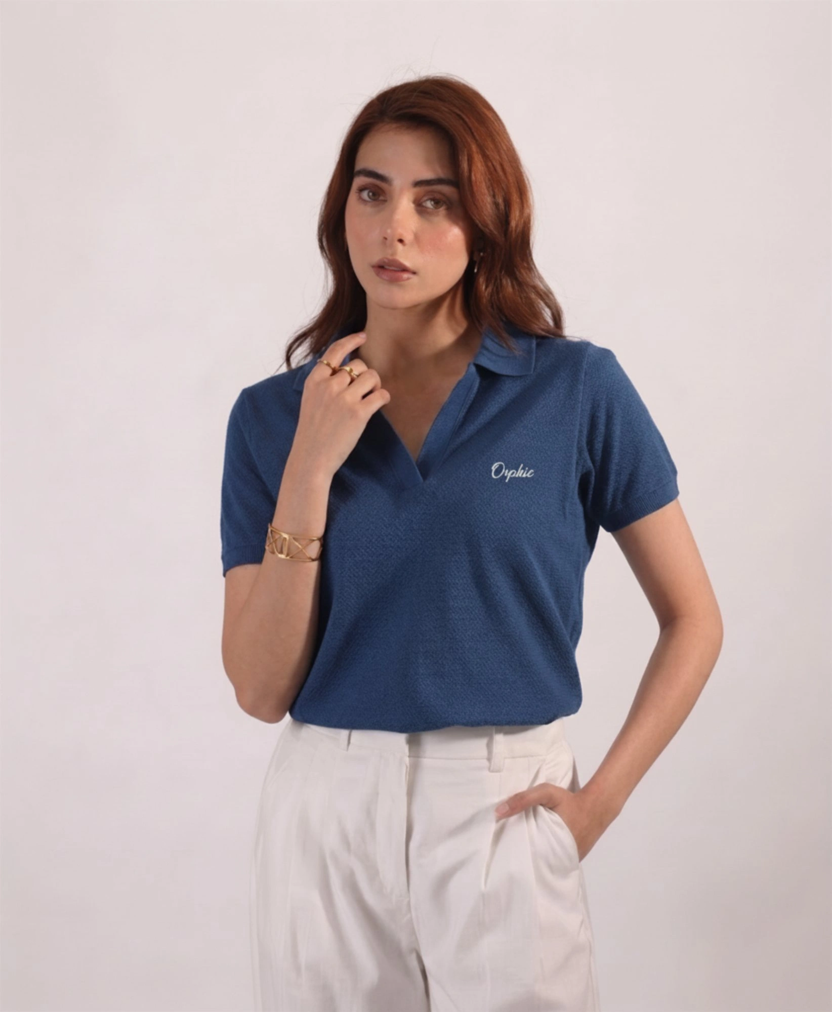 Woman wearing Orphic denim blue open-collar polo with cream embroidery, front view
